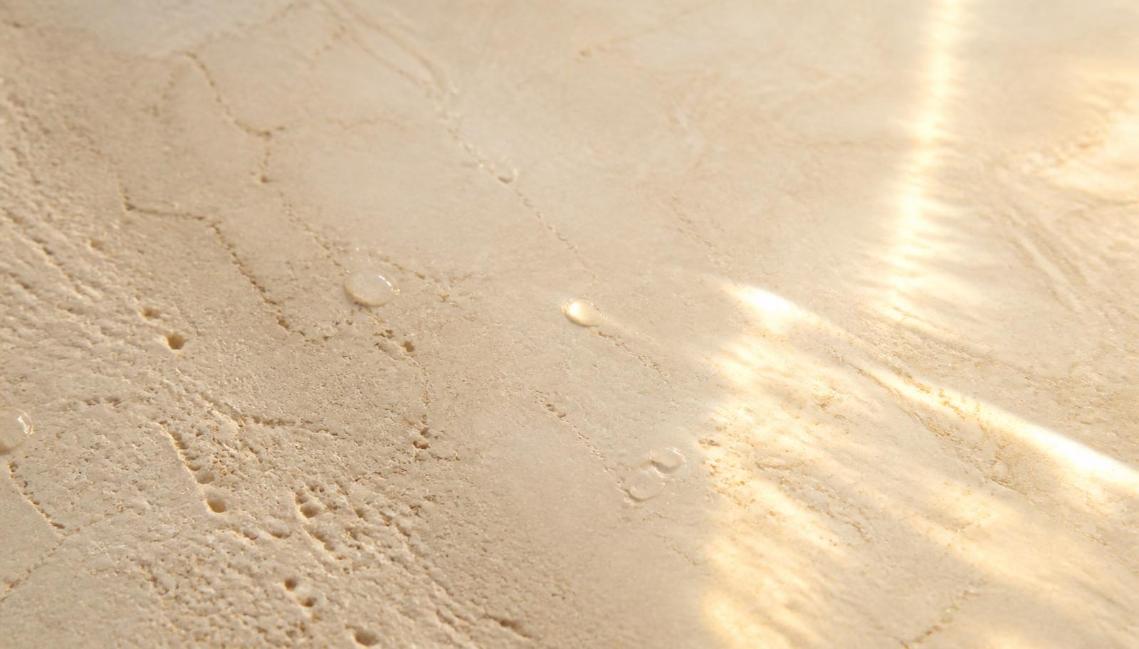 Sunlit travertine marble surface with water droplets